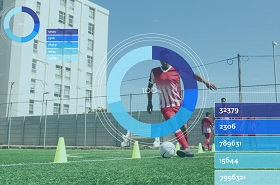 A soccer player in a red and white uniform dribbles a ball on a field with digital charts and stats overlay. The scene is bright and focused.