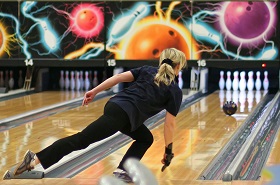 A person bowling in a vibrant alley with cosmic murals, releasing a ball towards pins.