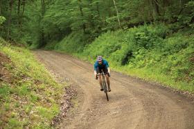 Man biking on a dirt trail with trees and grass in background