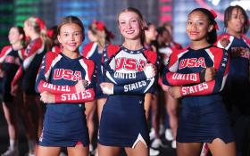 Cheerleaders in uniform stand on stage with medals around their necks, under a FISU World University Championship banner.