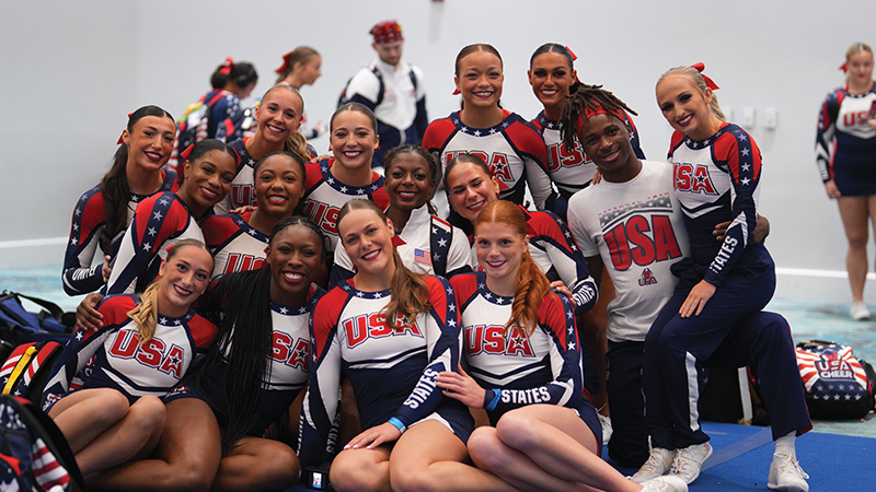 A diverse group of cheerleaders in USA uniforms smiles together for a photo.